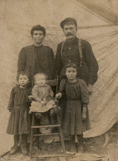 Bertha and William Henry with their young children, Katie, baby John, and Ellen, in front of a blank canvas backdrop
