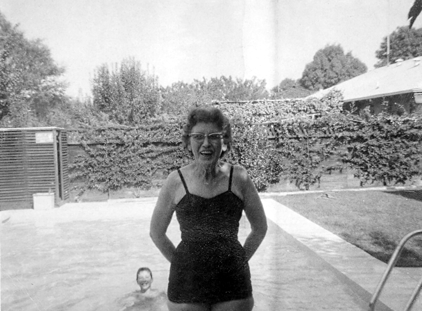 Katie in a bathing suit by a pool, a boy swimming in the background