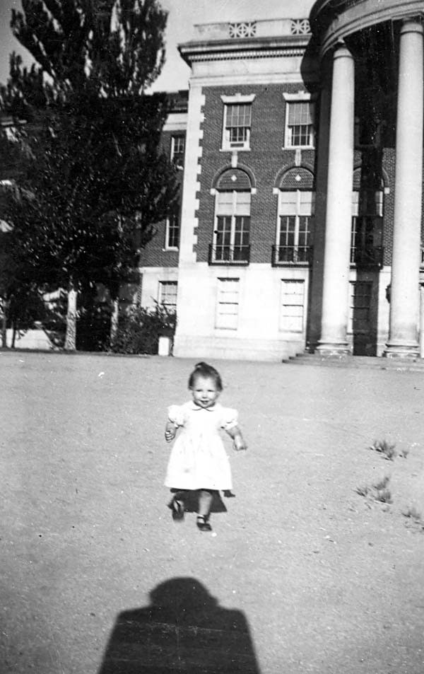 Janice as baby, running in front of a building